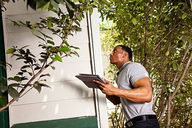 A property inspector checking the exterior of a house, tablet in hand